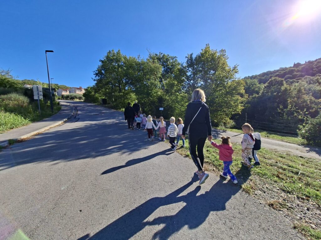 Otroci se sprehajajo z vzgojiteljicami po robu ceste