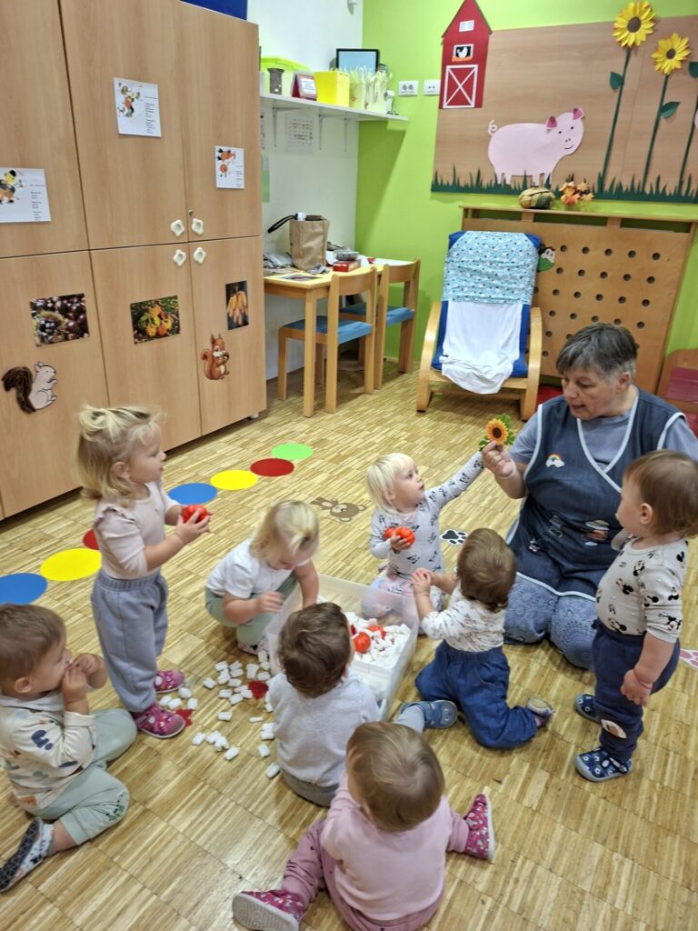 Vzgojiteljica z otroki okoli škatle v igralnici vrtca.