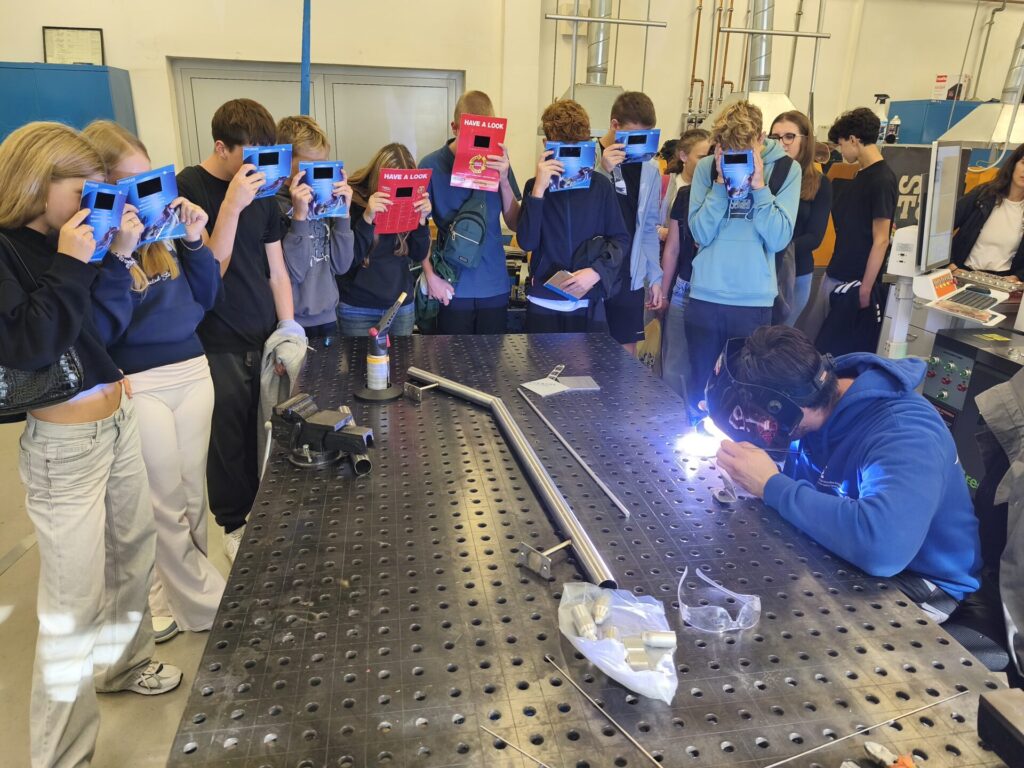 Učenci preko zaščitnih mask si ogledujejo TIG varjenje.